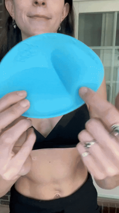 Woman inserting a blue Honeycloudz bra pad into her black sports bra