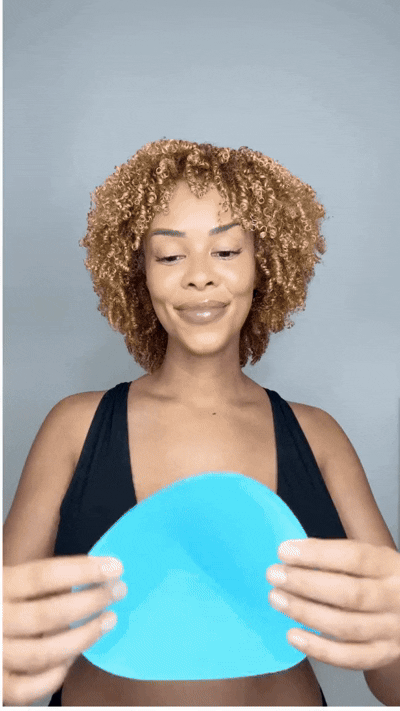 Woman holding a blue Honeycloudz bra pad insert before placing it into a sports bra.