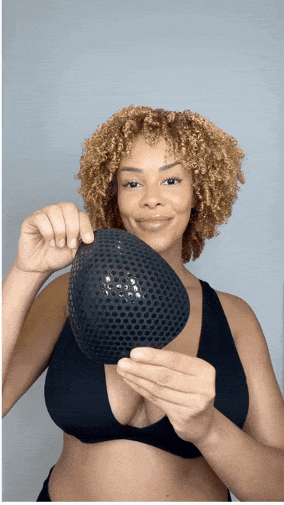 Woman inserting a blue Honeycloudz bra pad into her black sports bra