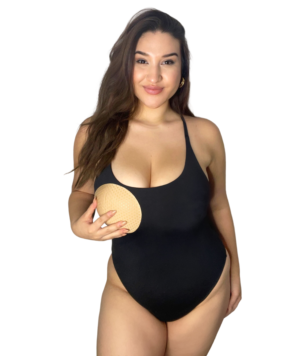 Woman in black swimsuit holding a beige bra insert, demonstrating body confidence and supportive fit.
