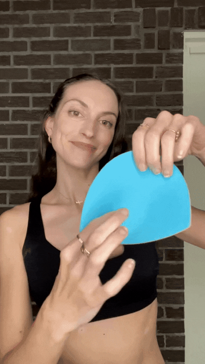 Woman holding a blue Honeycloudz bra pad insert before placing it into a sports bra.
