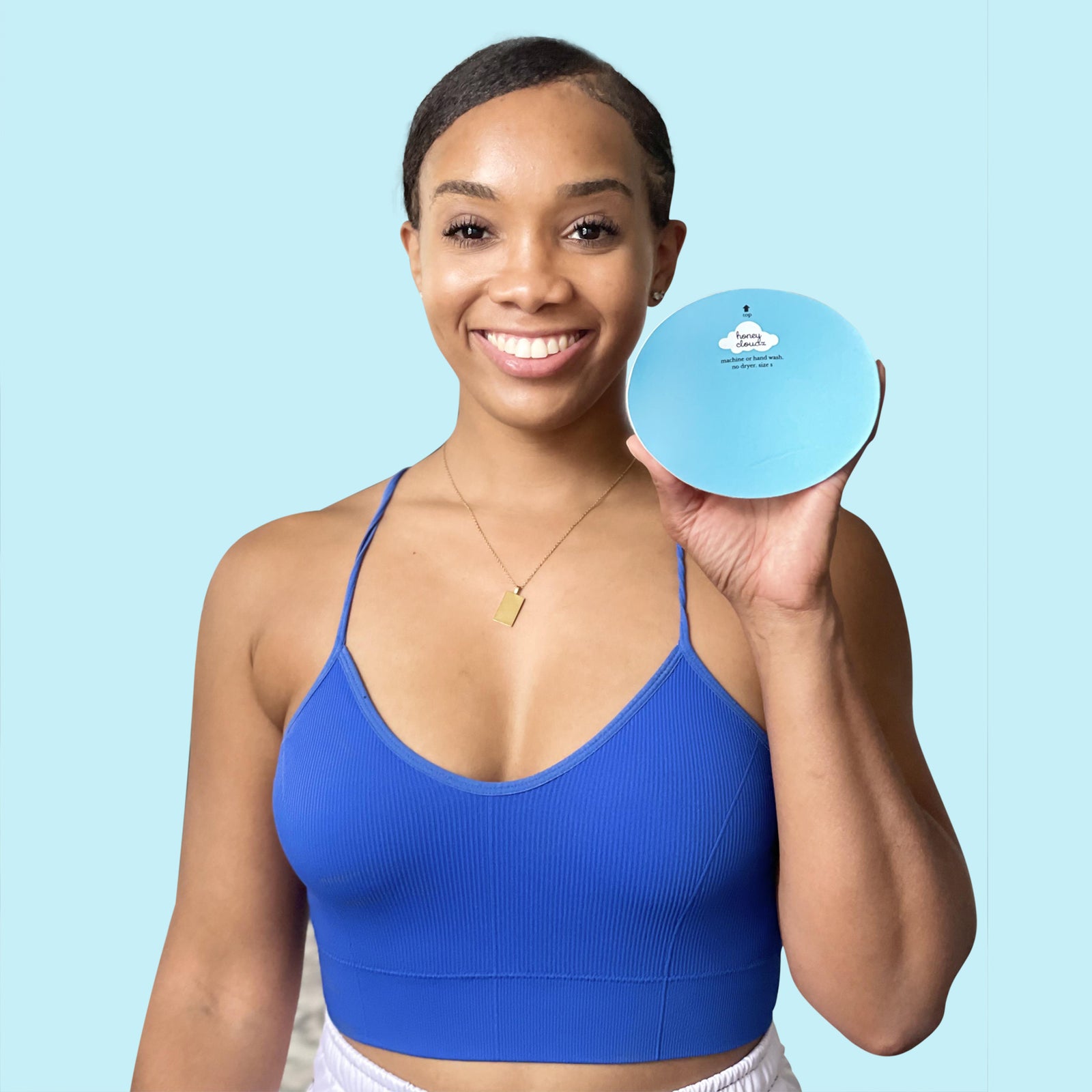Woman in blue sports bra holding a round product box with bra insert, promoting reusable and washable design.