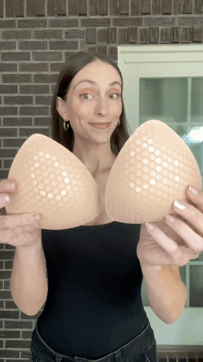 Woman holding a blue Honeycloudz bra pad insert before placing it into a sports bra.
