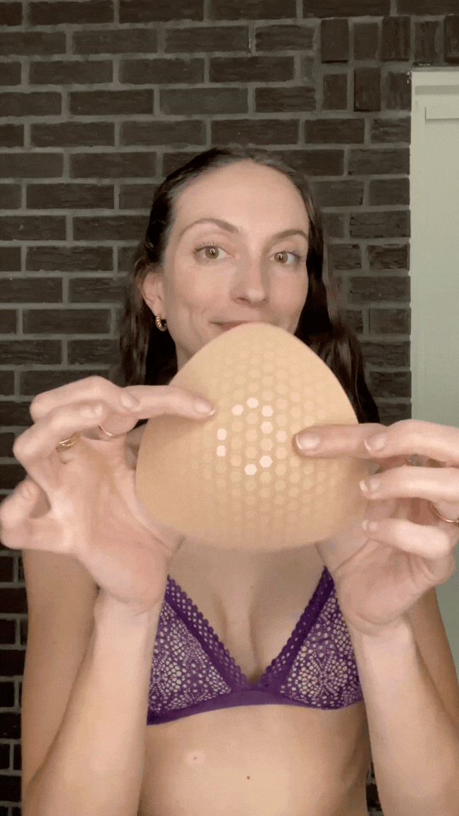 Woman holding a blue Honeycloudz bra pad insert before placing it into a sports bra.