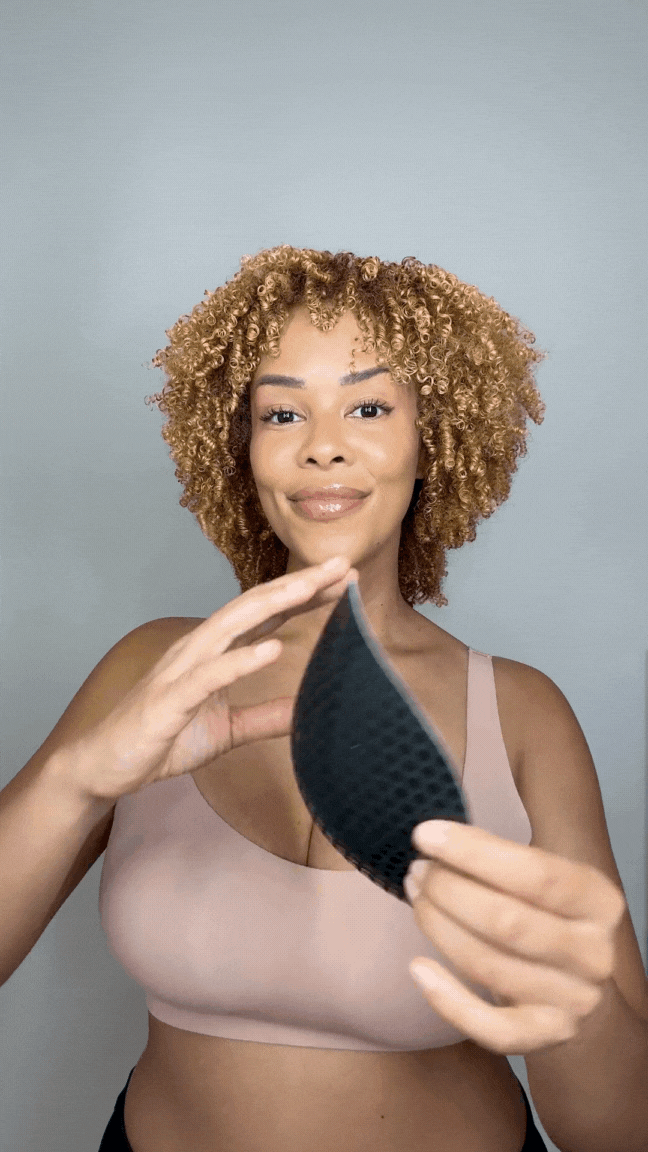 Woman holding a blue Honeycloudz bra pad insert before placing it into a sports bra.